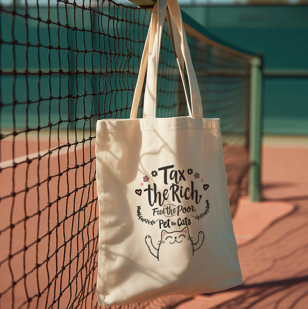 A natural-colored cotton canvas tote bag featuring a bold pink design with a cartoon cat illustration and the phrase “Tax the Rich, Feed the Poor, Pet the Cats.” The artwork is printed on the front side of the bag, which measures 15 inches by 16 inches. The bag includes two sturdy handles for carrying and is made from eco-friendly cotton material, designed for everyday use as a book tote, protest bag, or gift for anti-capitalist cat lovers.
